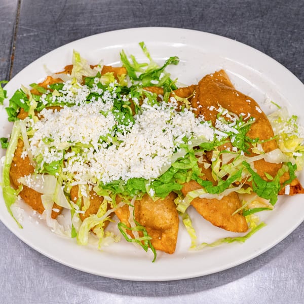 A white oval plate filled with golden-brown fried quesadillas, topped with shredded lettuce and crumbled white cheese.