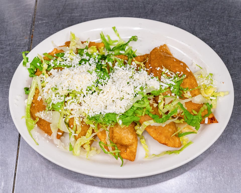 A white oval plate filled with golden-brown fried quesadillas, topped with shredded lettuce and crumbled white cheese.