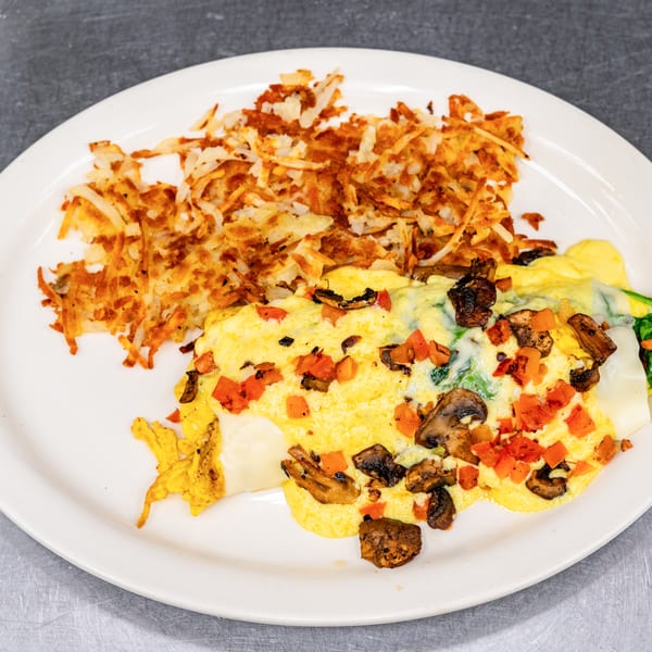 A fluffy omelet filled with mushrooms, spinach, and cheese, served with a side of crispy hash browns.