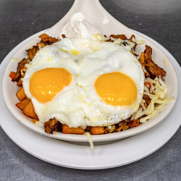 Breakfast skillet with fried eggs, potatoes, chorizo, shredded cheese, and a dollop of sour cream.