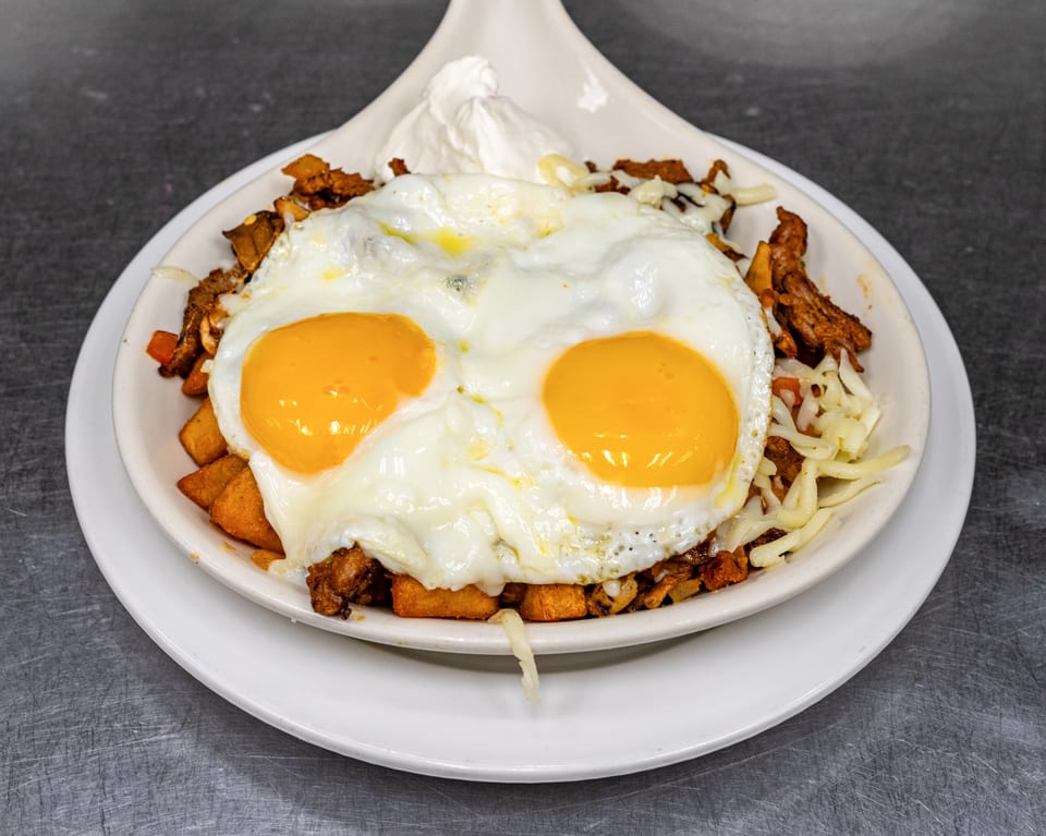 Breakfast skillet with two sunny-side-up eggs, potatoes, chorizo, cheese, and a dollop of sour cream.