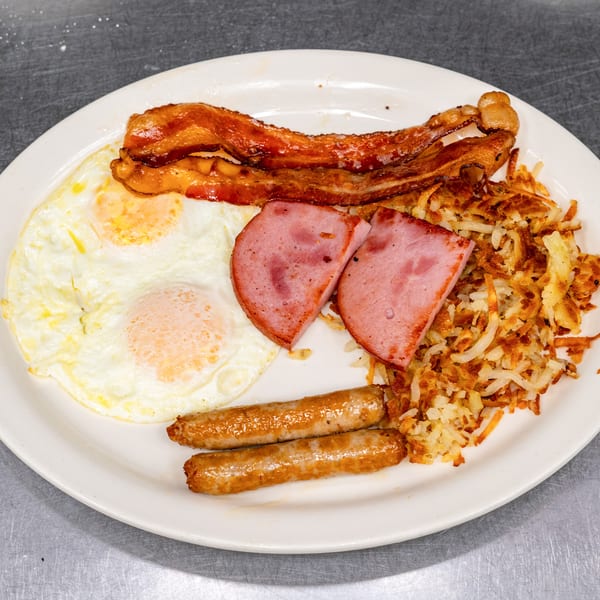 A full breakfast plate with fried eggs, bacon, ham, sausage links, and hash browns.