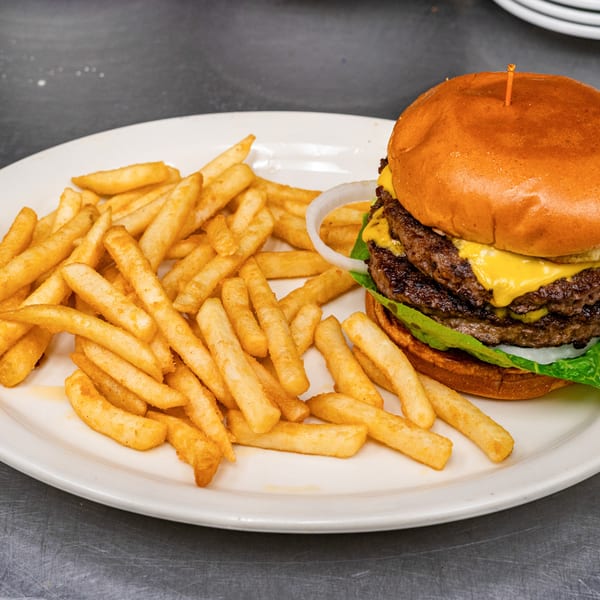 A double cheeseburger with lettuce, onion, and fries on a white plate.