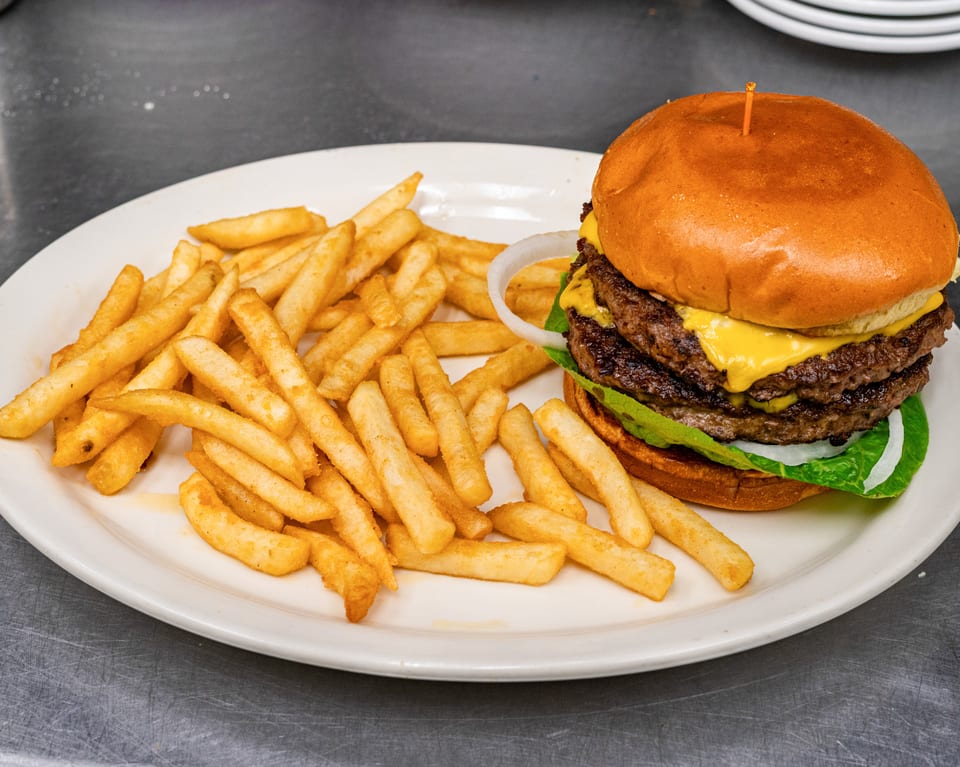 A double cheeseburger with lettuce, onion, and fries on a white plate.