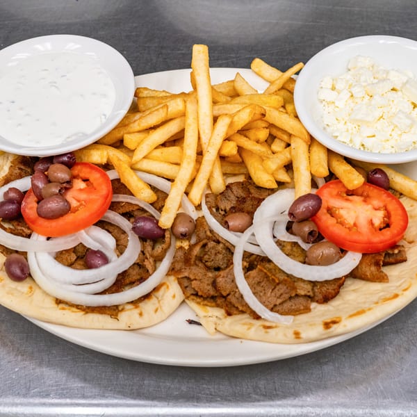 Two gyros with meat, onions, tomatoes, olives, fries, tzatziki, and feta cheese on a plate.