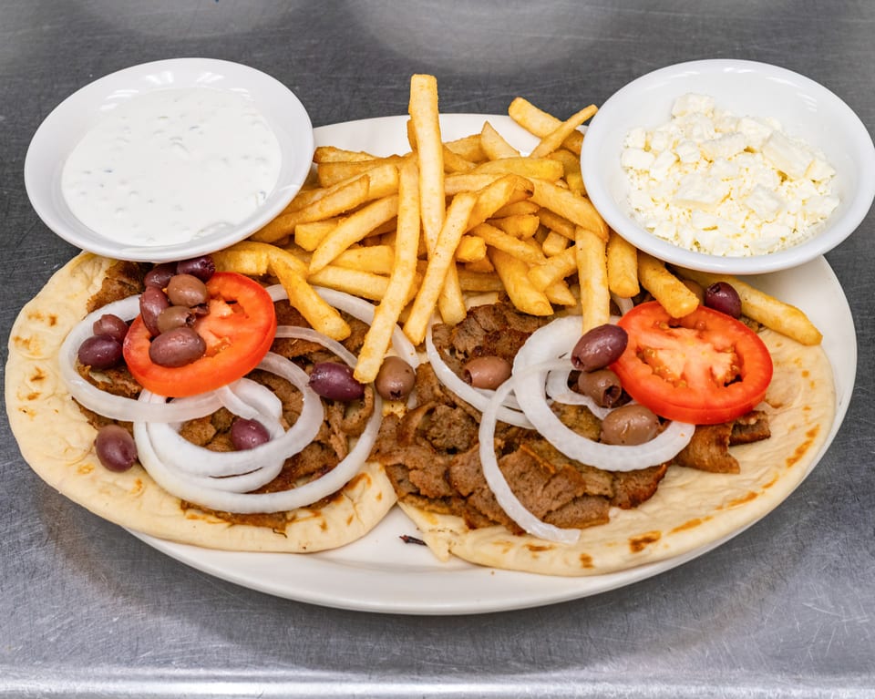 Two gyros with meat, onions, tomatoes, olives, fries, tzatziki, and feta cheese on a plate.