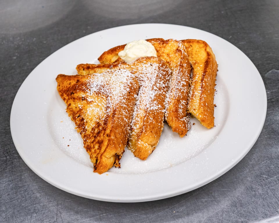 Golden French toast slices, dusted with powdered sugar and topped with a dollop of butter.