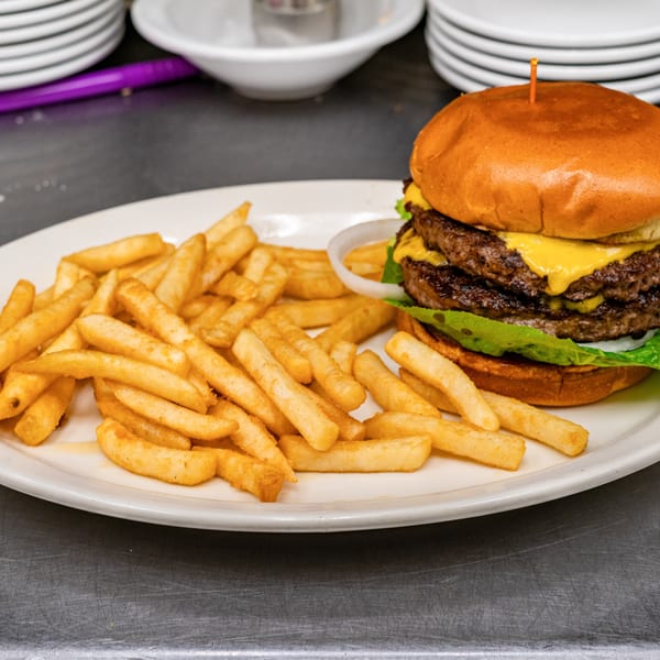 Double cheeseburger with lettuce, onion, and fries on a white plate.