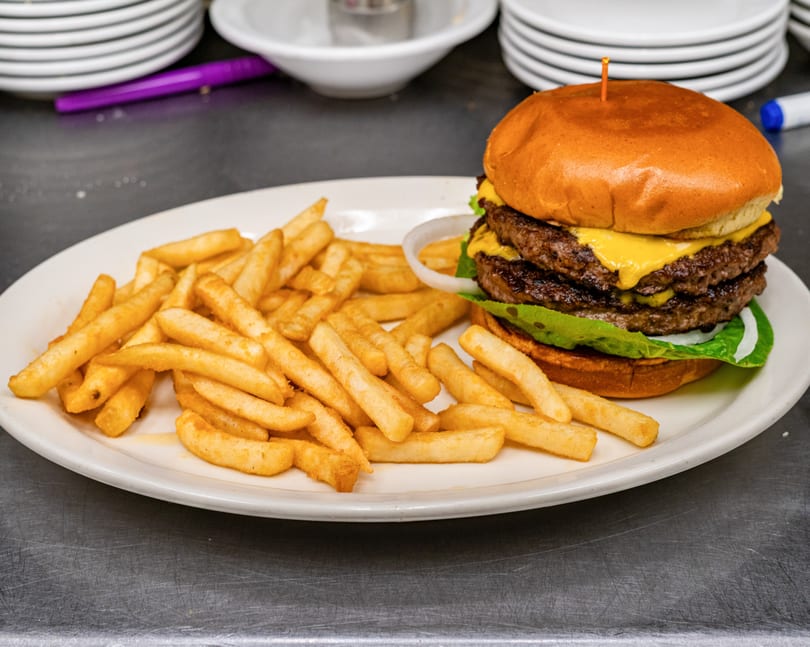 Double cheeseburger with lettuce, onion, and fries on a white plate.