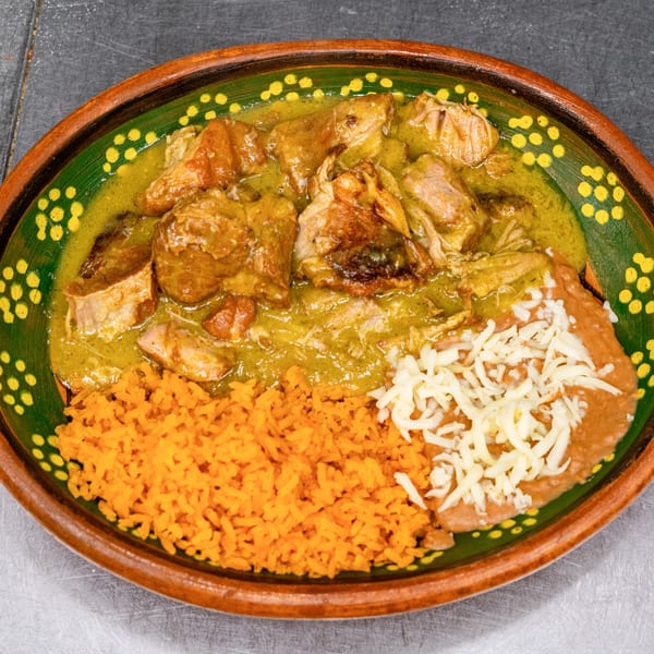 Pork in green chile sauce with orange rice and refried beans topped with cheese in a decorative bowl.