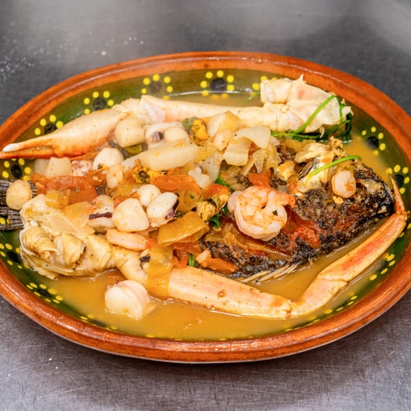 Whole fried fish with crab legs, shrimp, and vegetables in a savory broth, served in a decorative bowl.