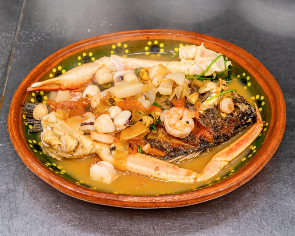 Whole fried fish with crab legs, shrimp, and vegetables in a savory broth, served in a decorative bowl.